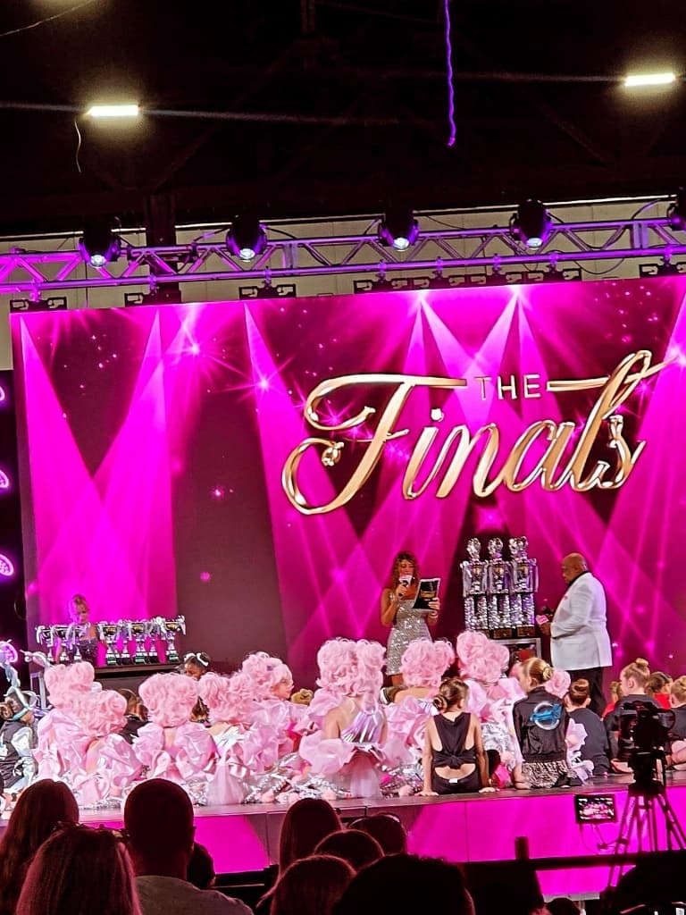 Young dancers in pink costumes seated on stage during the awards at The Finals national dance competition